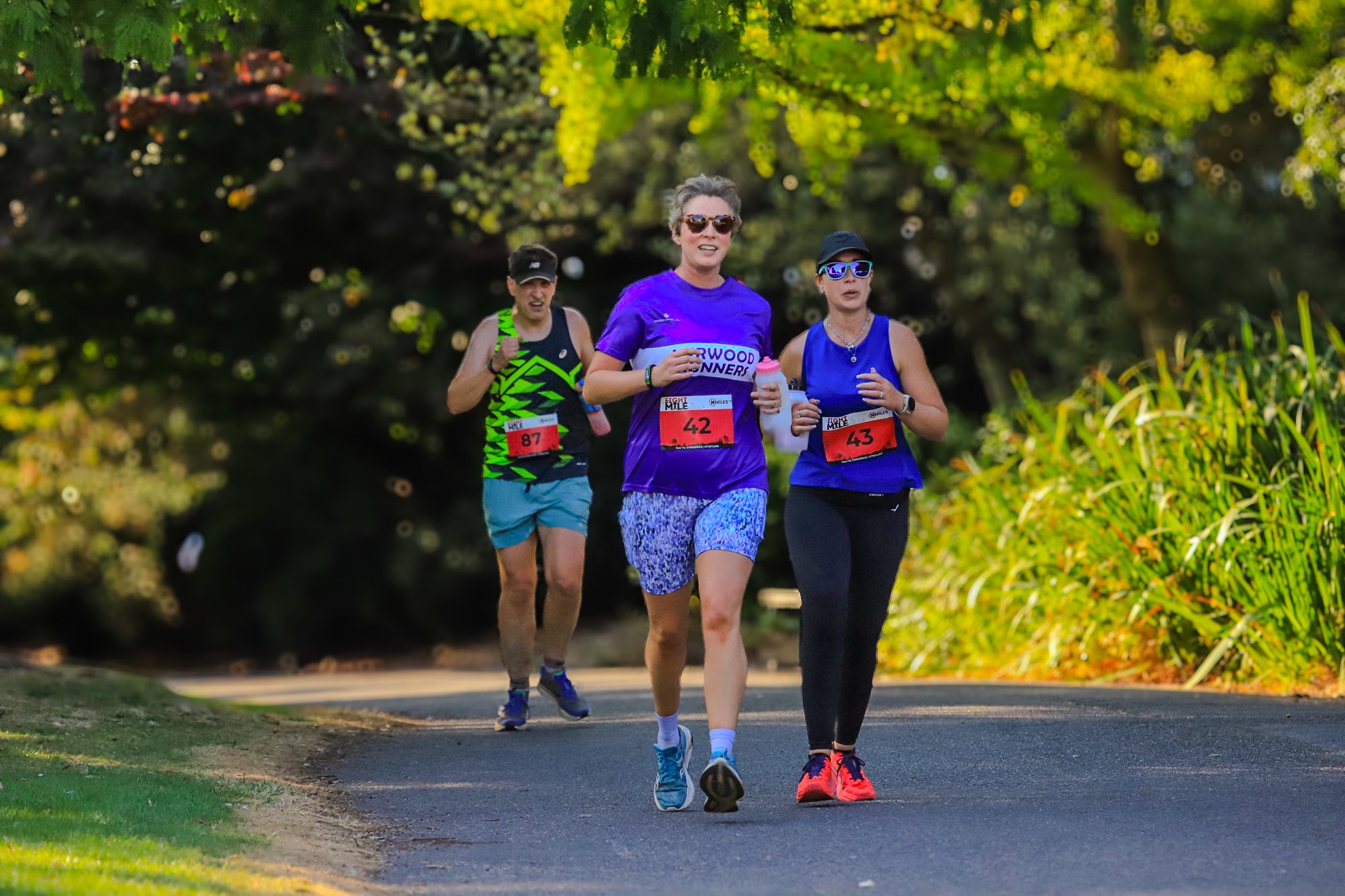 Three runners in colourful club vests on the sunlit course — Jess Photography