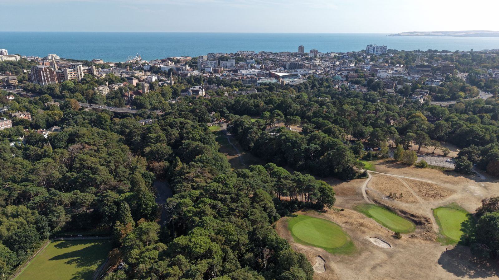 Wide aerial of Meyrick Park pines and golf greens with the sea beyond